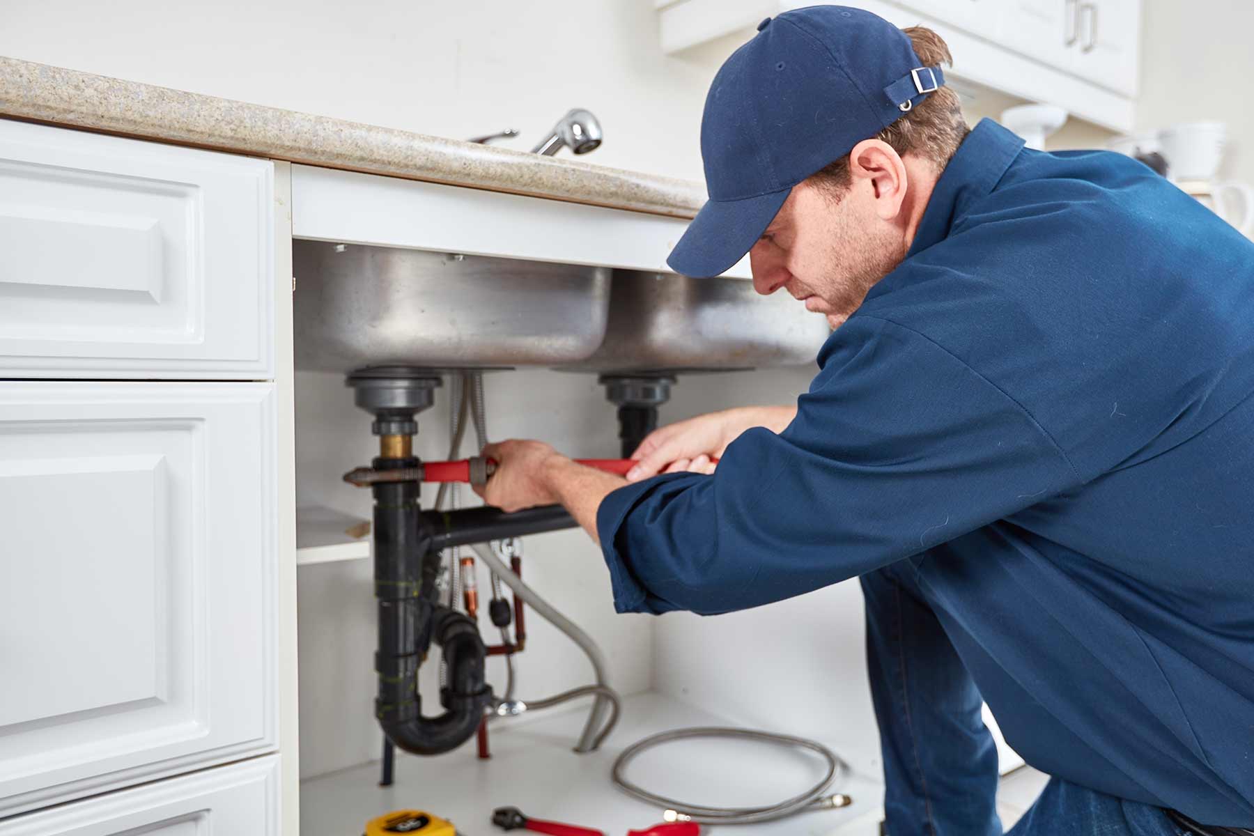 Professional plumber repairing pipes under a kitchen sink