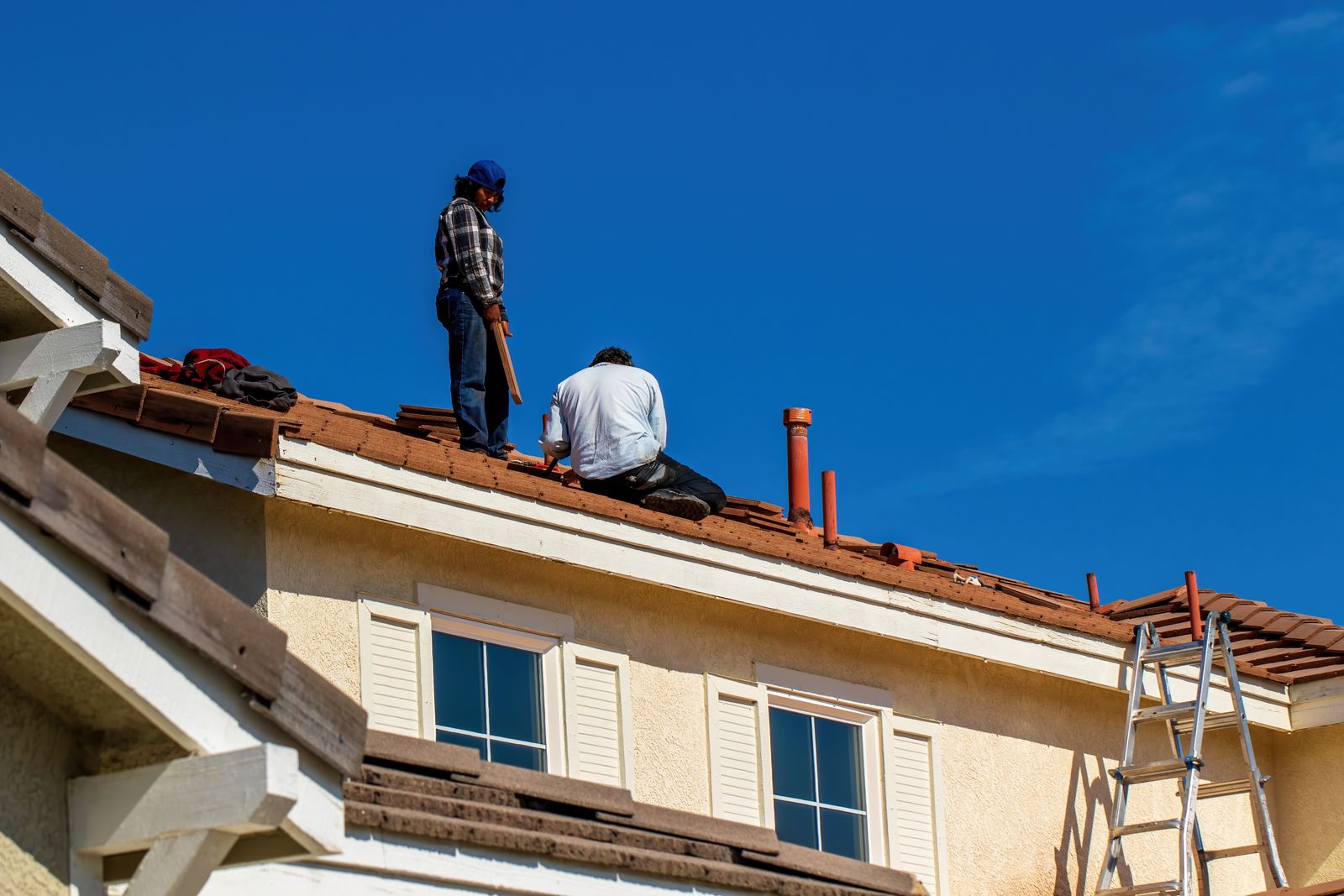 Roofers installing new shingles on a home against a blue sky
